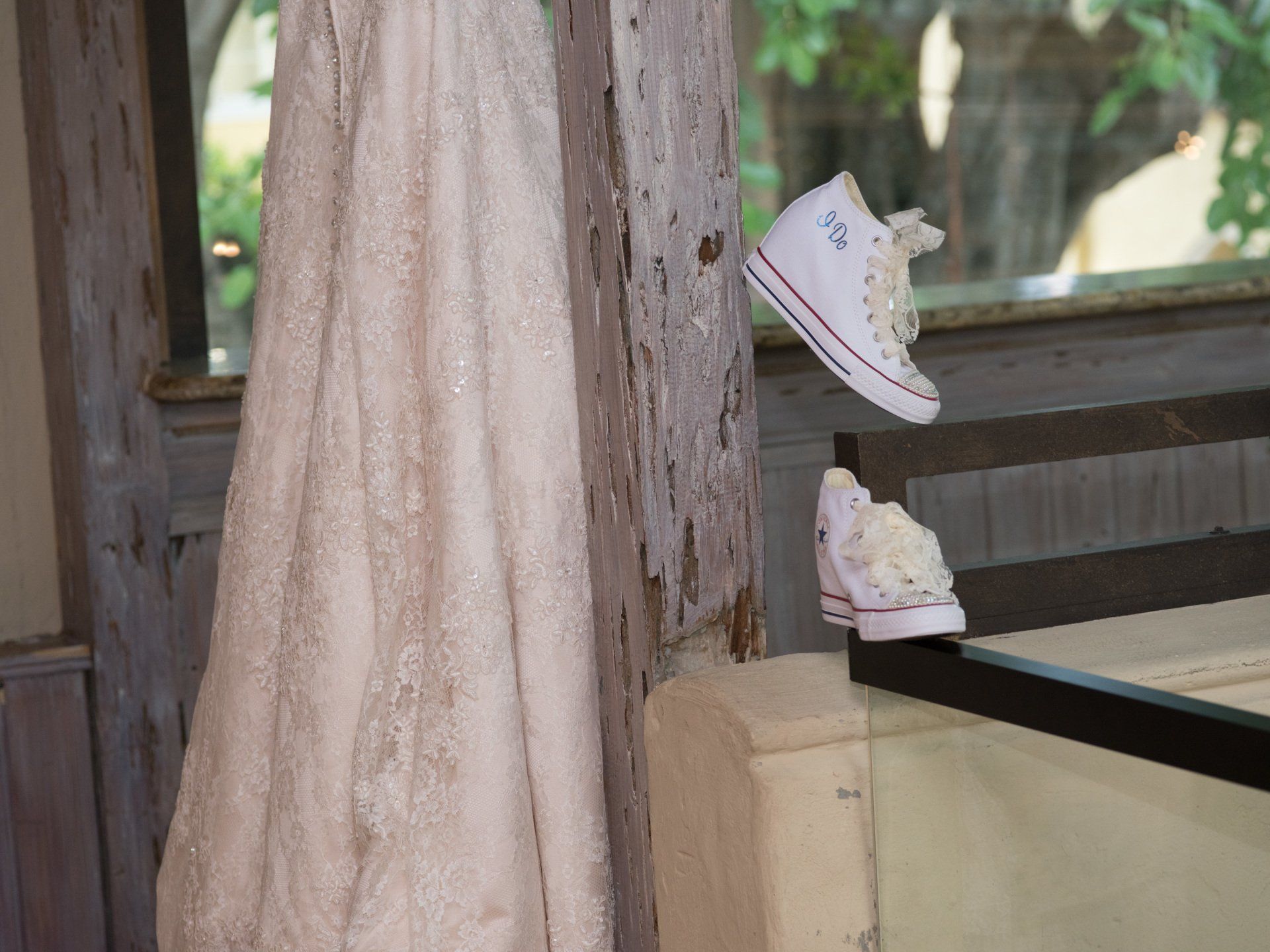 A wedding dress and converse shoes are hanging on a wooden post.