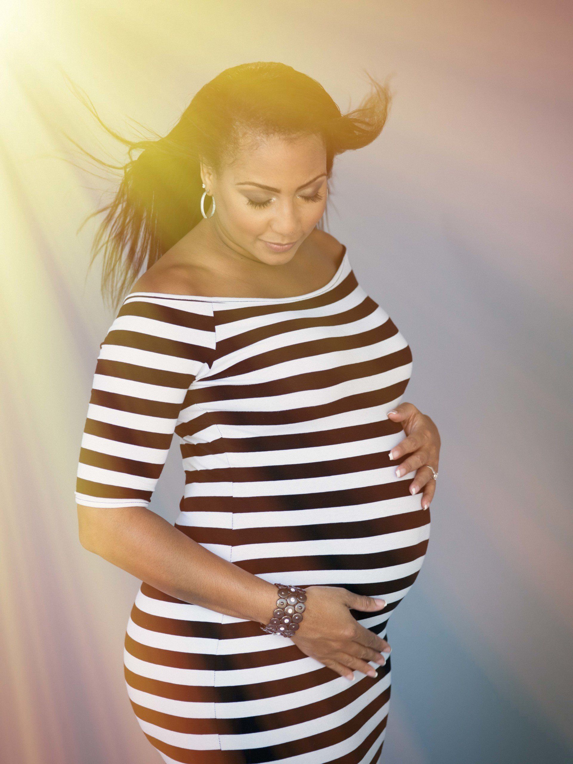 A pregnant woman in a striped dress is holding her belly.