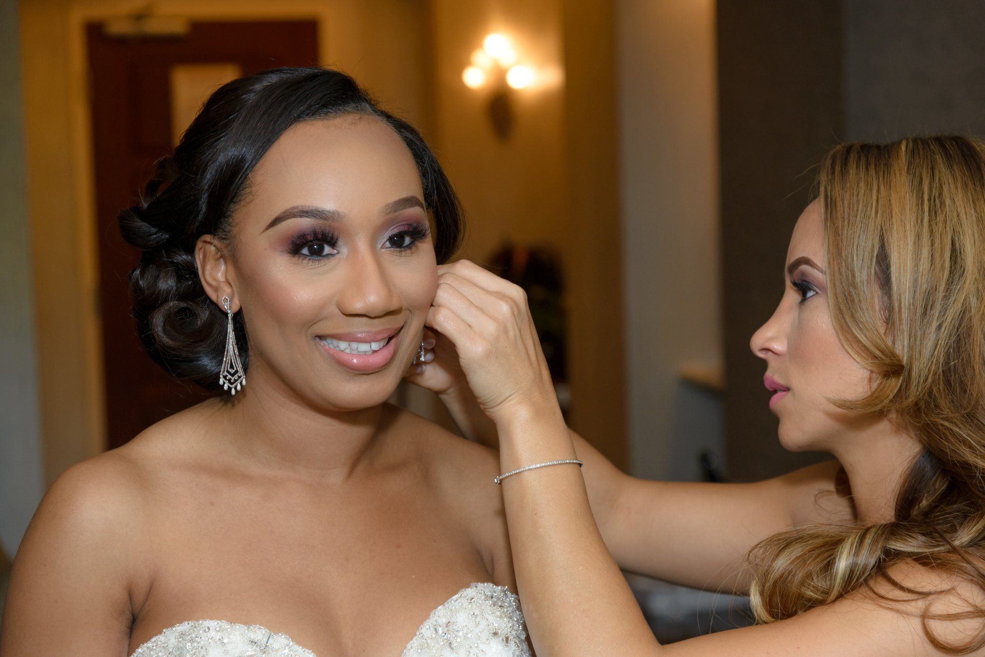 A woman is putting earrings on a bride 's ear.