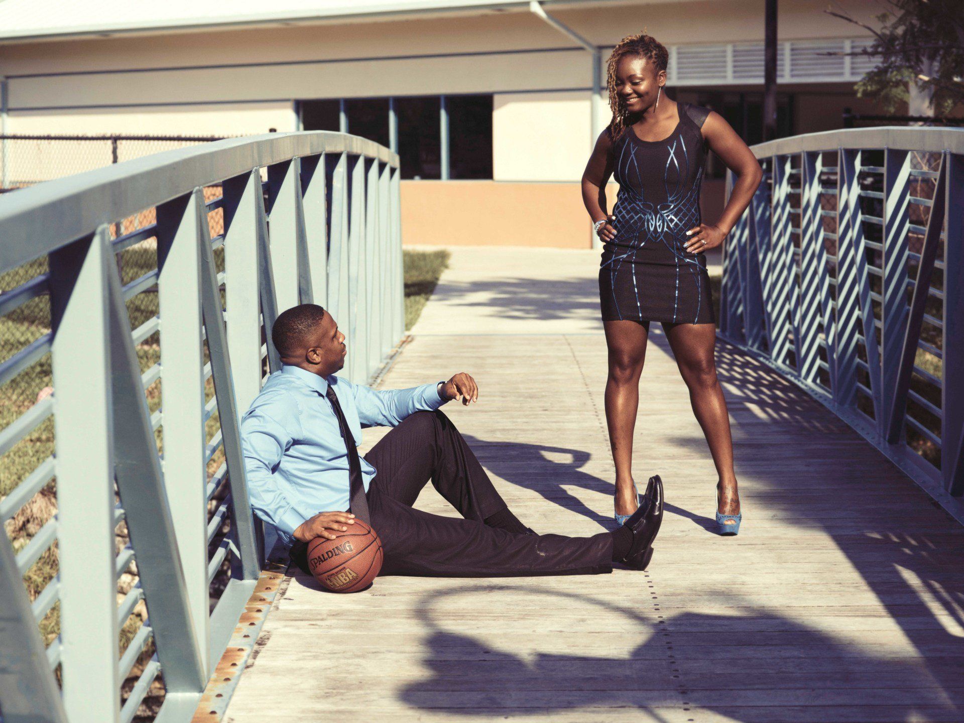 A man is laying on the ground holding a basketball while a woman stands behind him.
