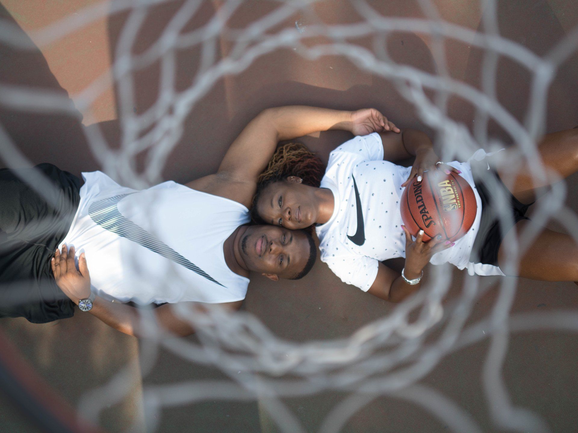 A man and a woman are laying in a basketball hoop.