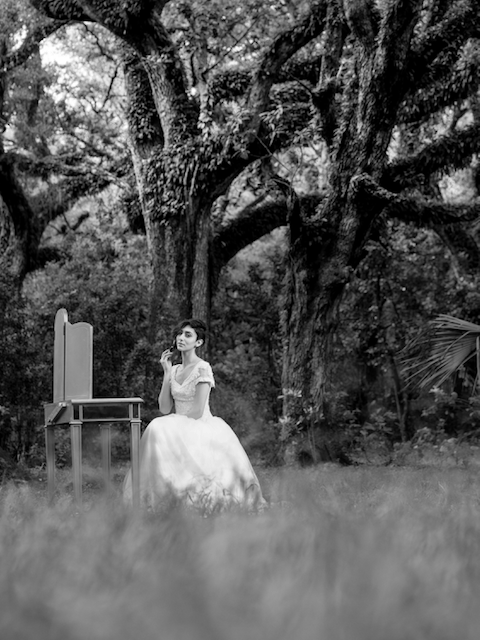 A woman in a white dress is sitting in a field under a tree.