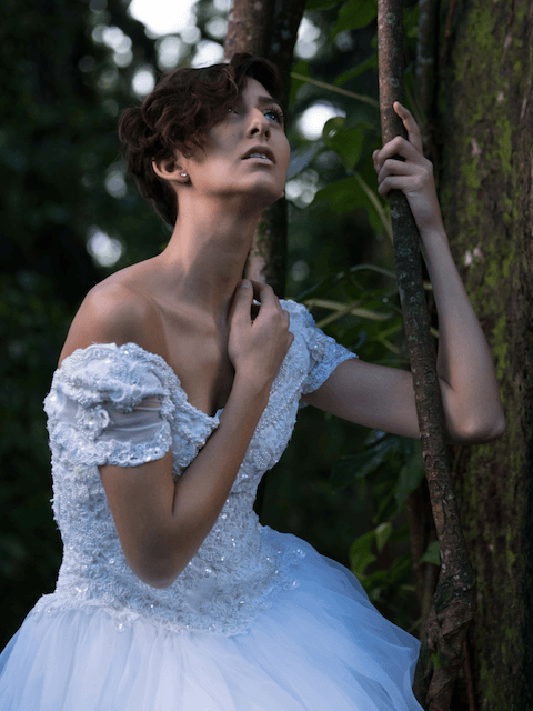 A woman in a white dress is standing next to a tree