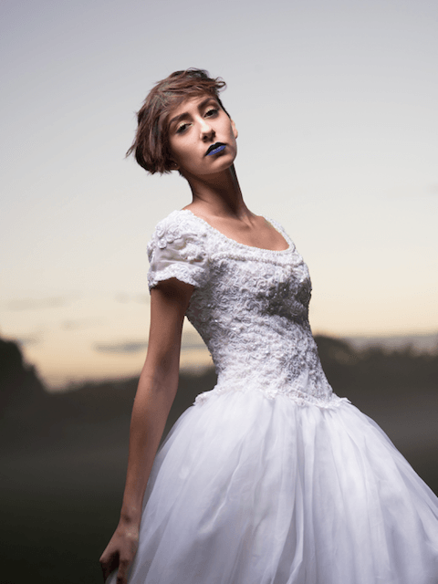 A woman in a white dress with blue lipstick is standing in a field.