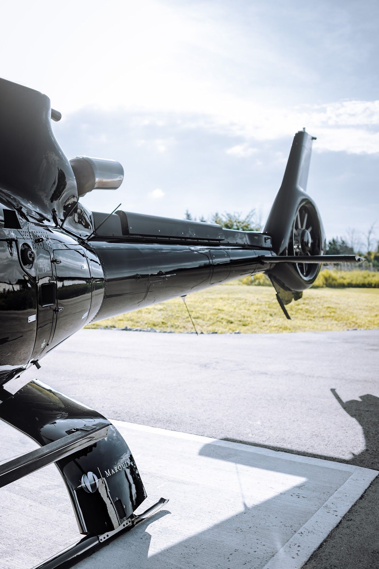 Black helicopter tail section on a tarmac, bright sky in the background.