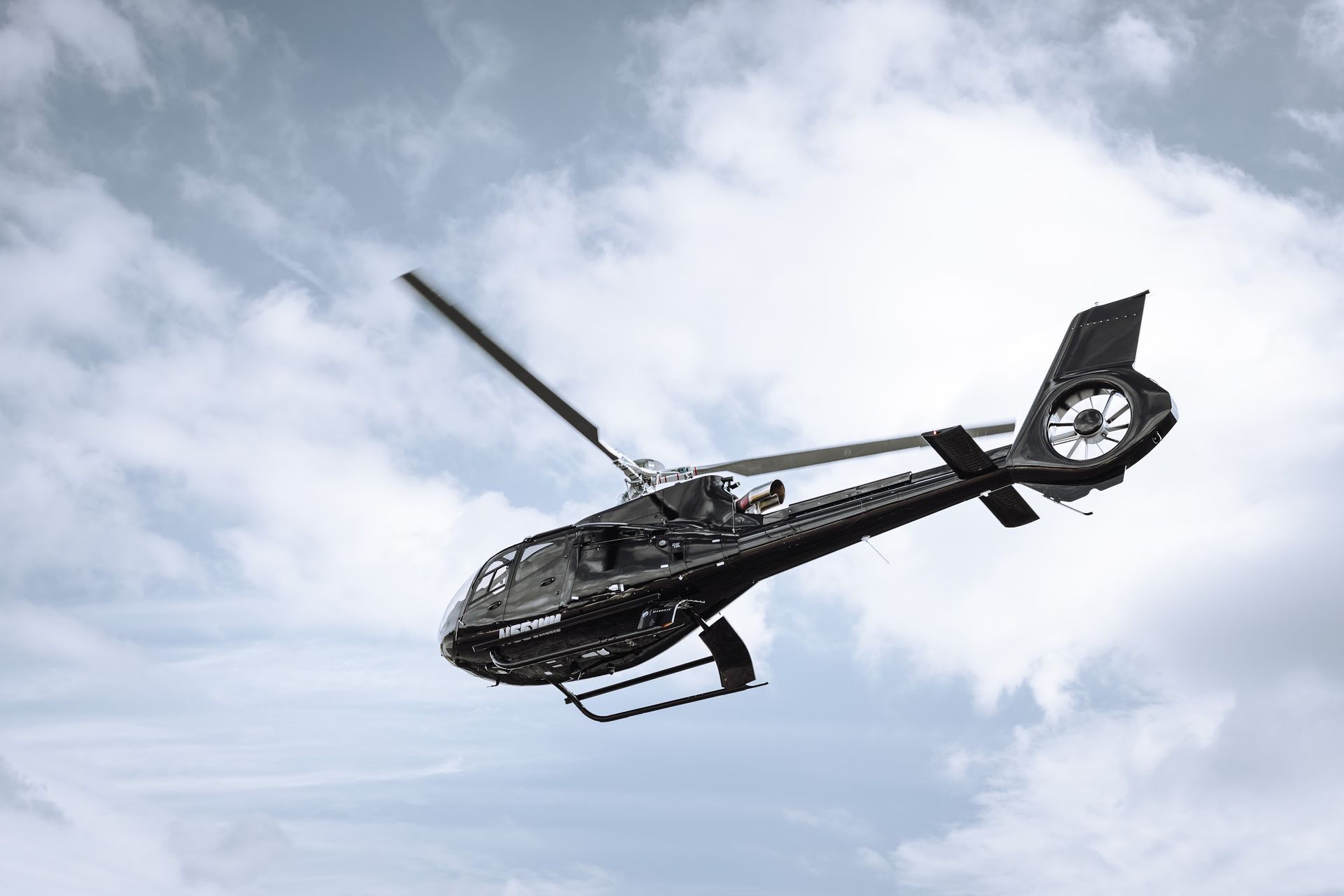 Black helicopter flying in a cloudy sky with spinning rotor blades.