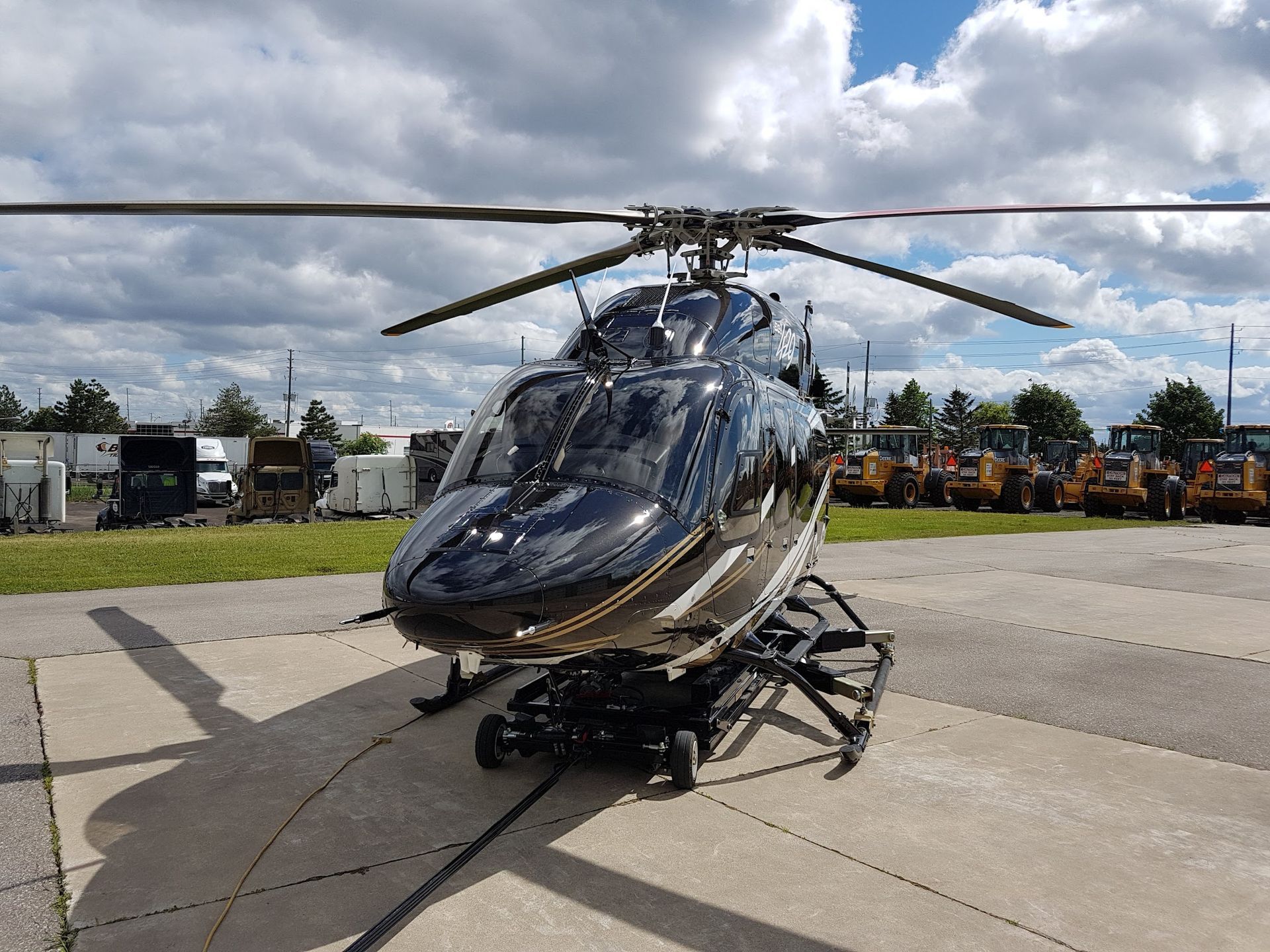 Black helicopter on a concrete surface with a backdrop of machinery and a cloudy sky.