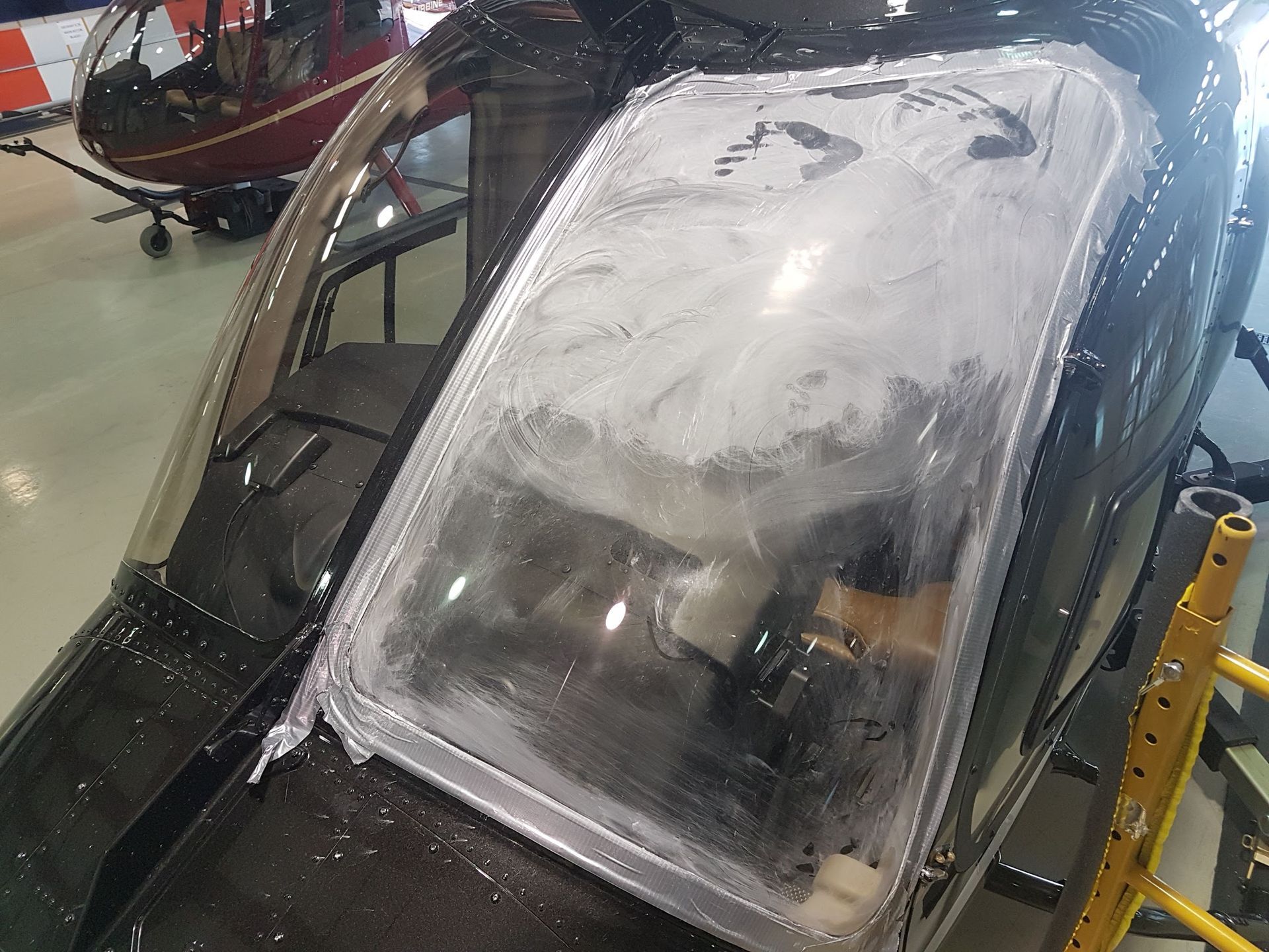 Helicopter cockpit with smeared, opaque windscreen, in a hangar.
