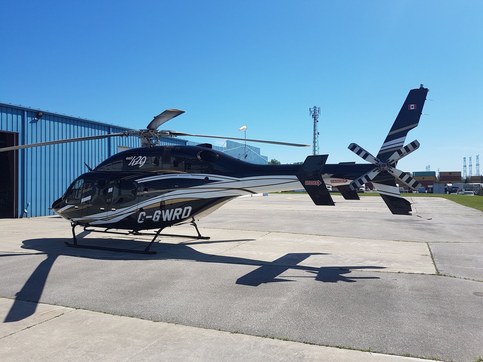 Black helicopter on a concrete pad with blue building in the background, under a blue sky.