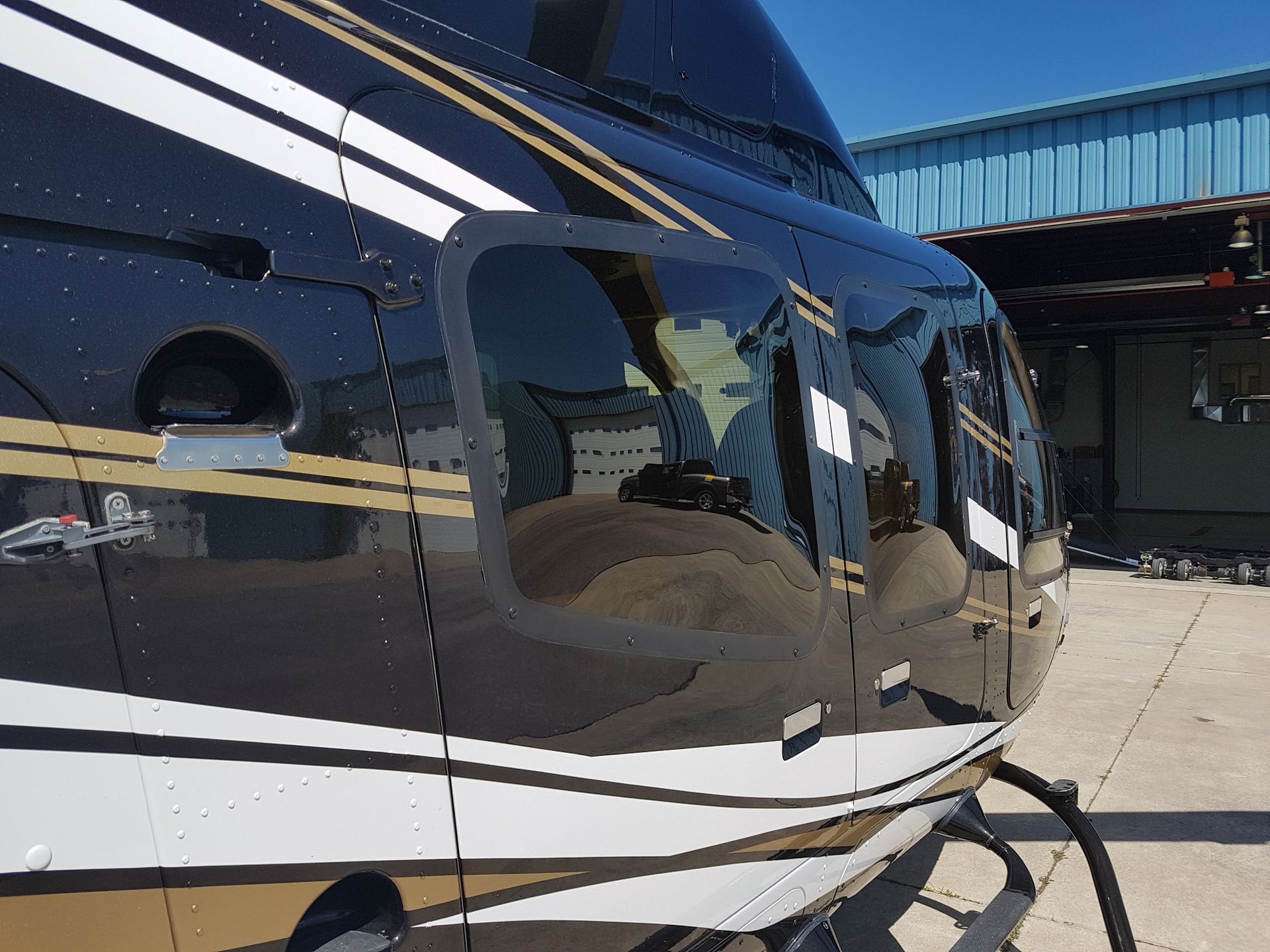 Black and gold helicopter side with windows, parked on a concrete surface.