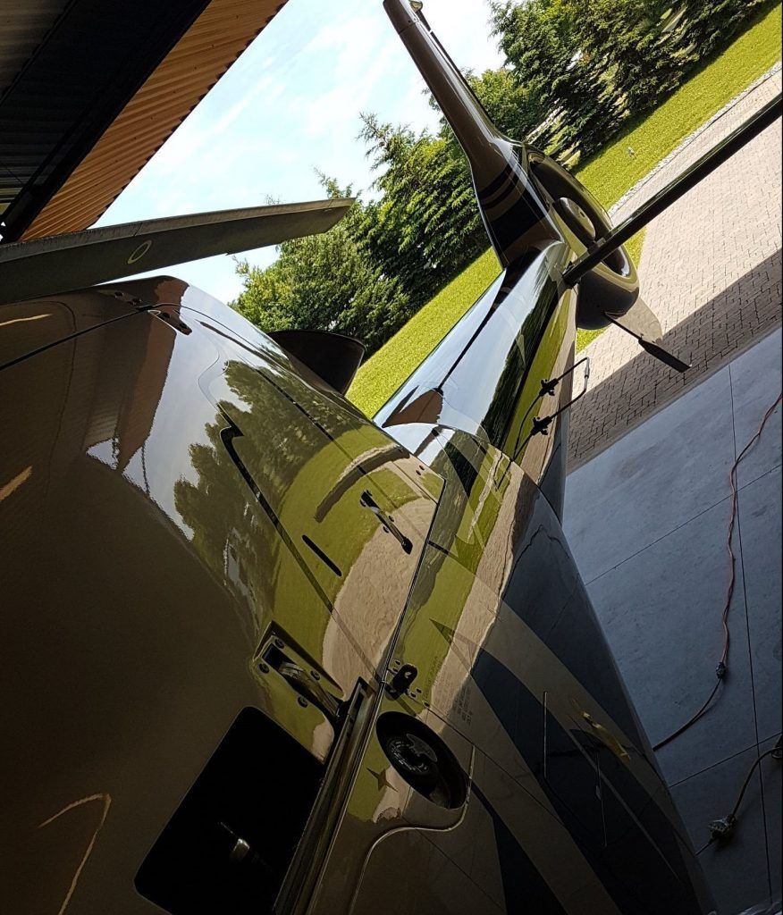 Close-up of a sleek, black and silver airplane tail and fuselage, reflecting surrounding trees and sky.
