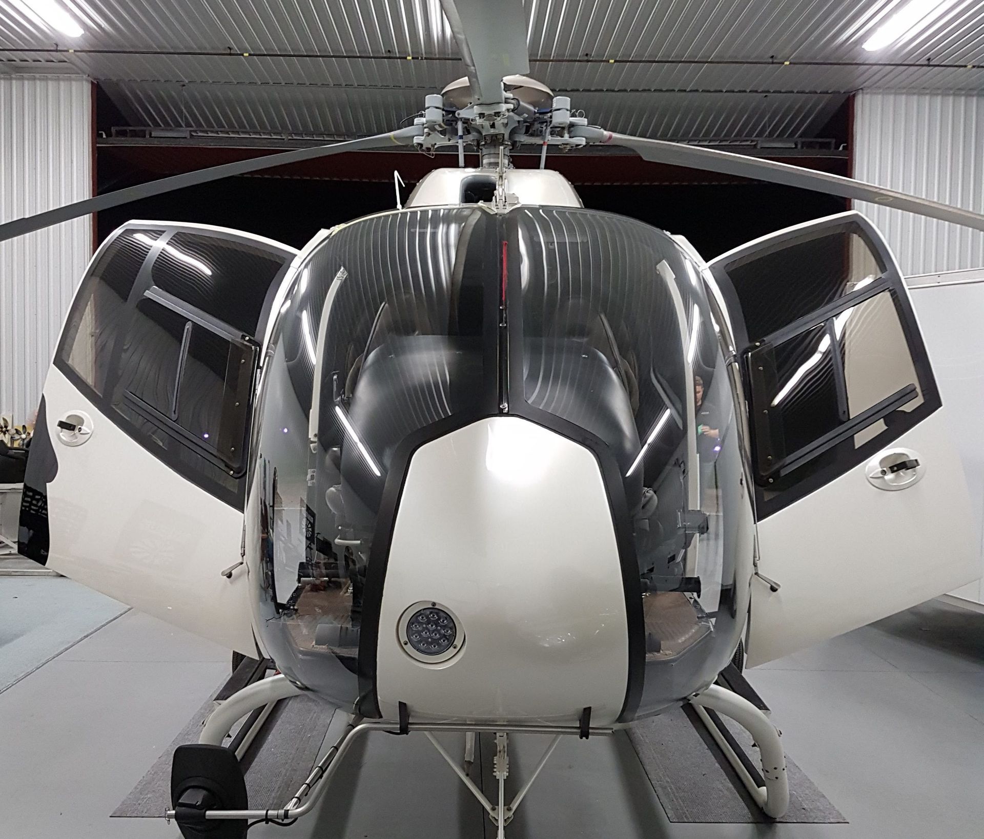 Helicopter with open doors, in a hangar. White, grey, and black.