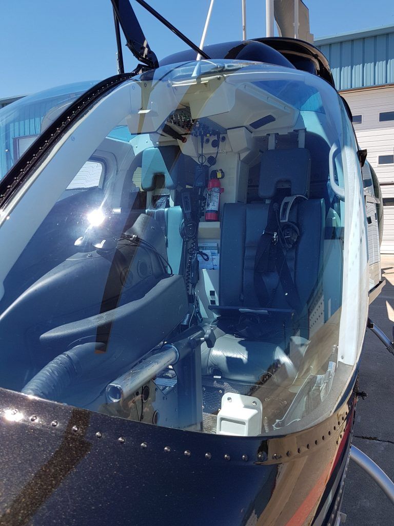 Helicopter cockpit interior: seats, controls, and equipment visible through clear, curved windows.