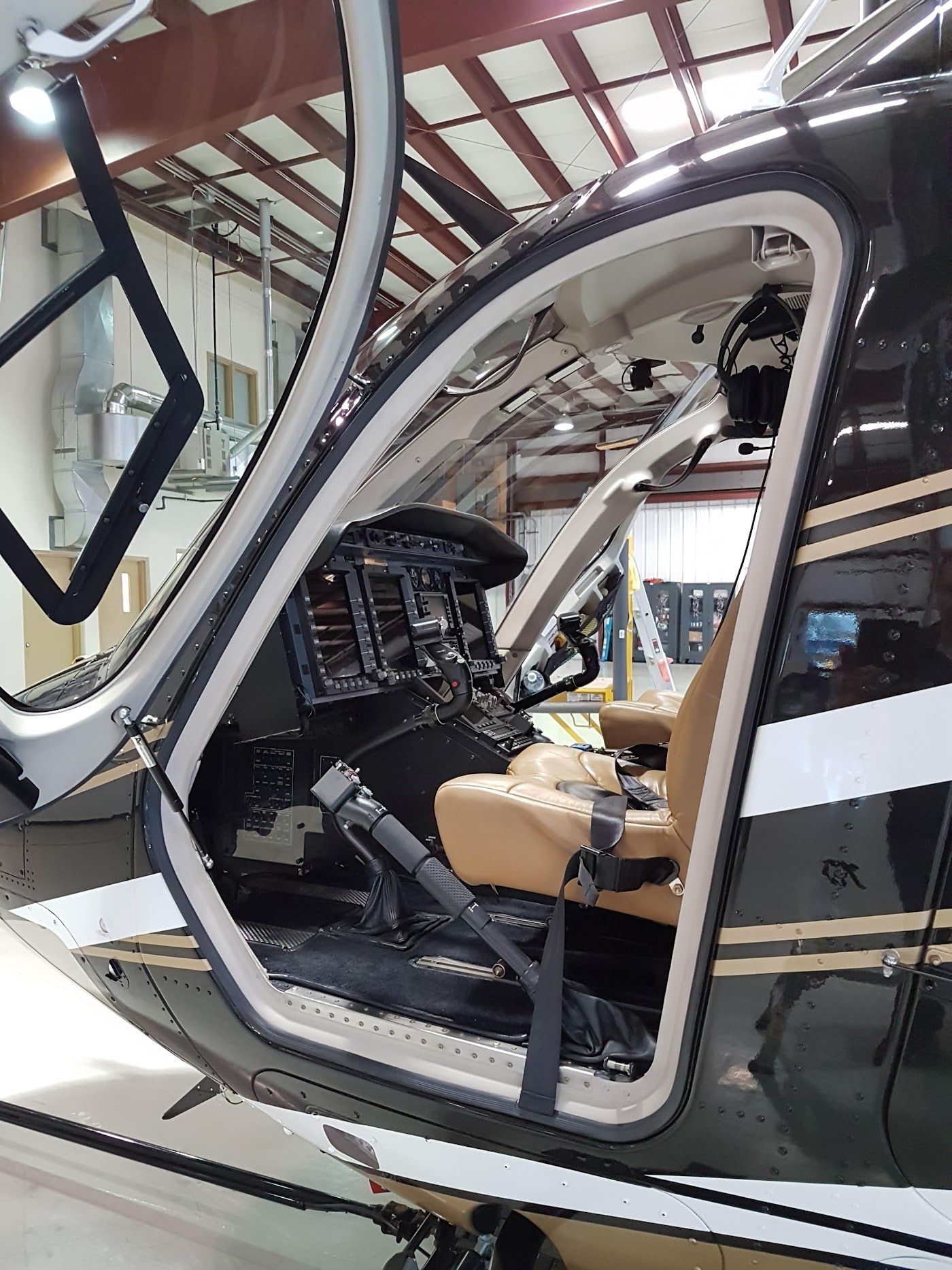 Black helicopter cockpit with open door, beige seat, control panel visible.