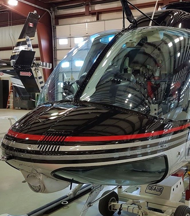 Black and silver helicopter nose, red stripe, in a hangar, reflective surfaces, front view.