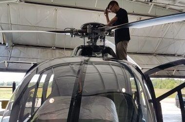 Mechanic inspecting helicopter rotor blades inside a hangar.