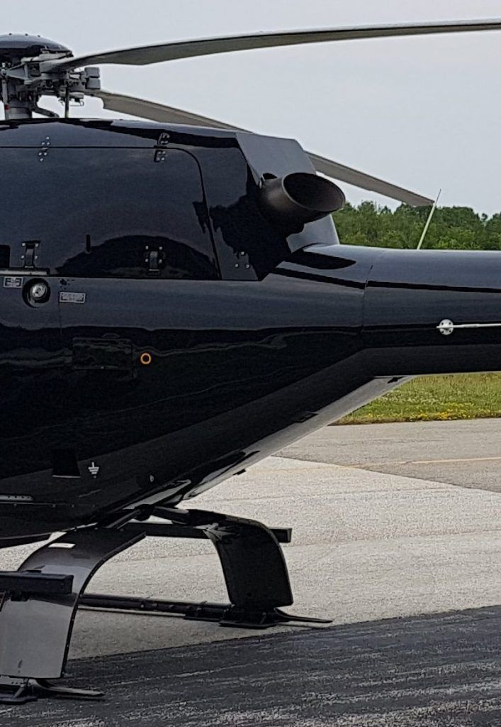 Black helicopter tail with a rotor and exhaust, on a gray surface outdoors.