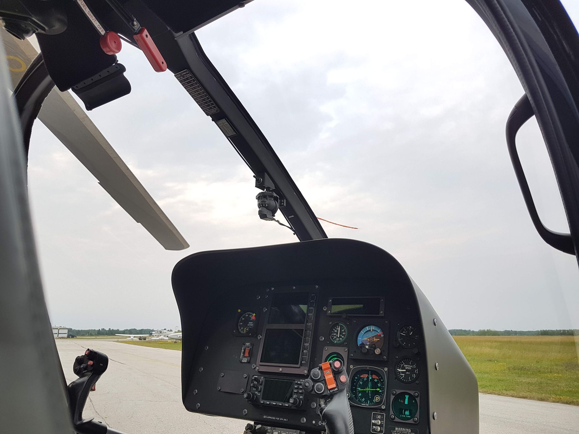 Helicopter cockpit view, overlooking a runway. Gray sky, instrument panel visible.