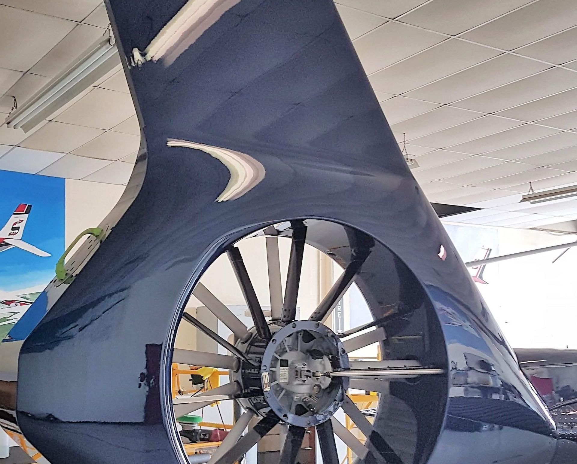 Close-up of a dark blue, ring-shaped airplane propeller within a cowling. Reflective surfaces in a hangar.