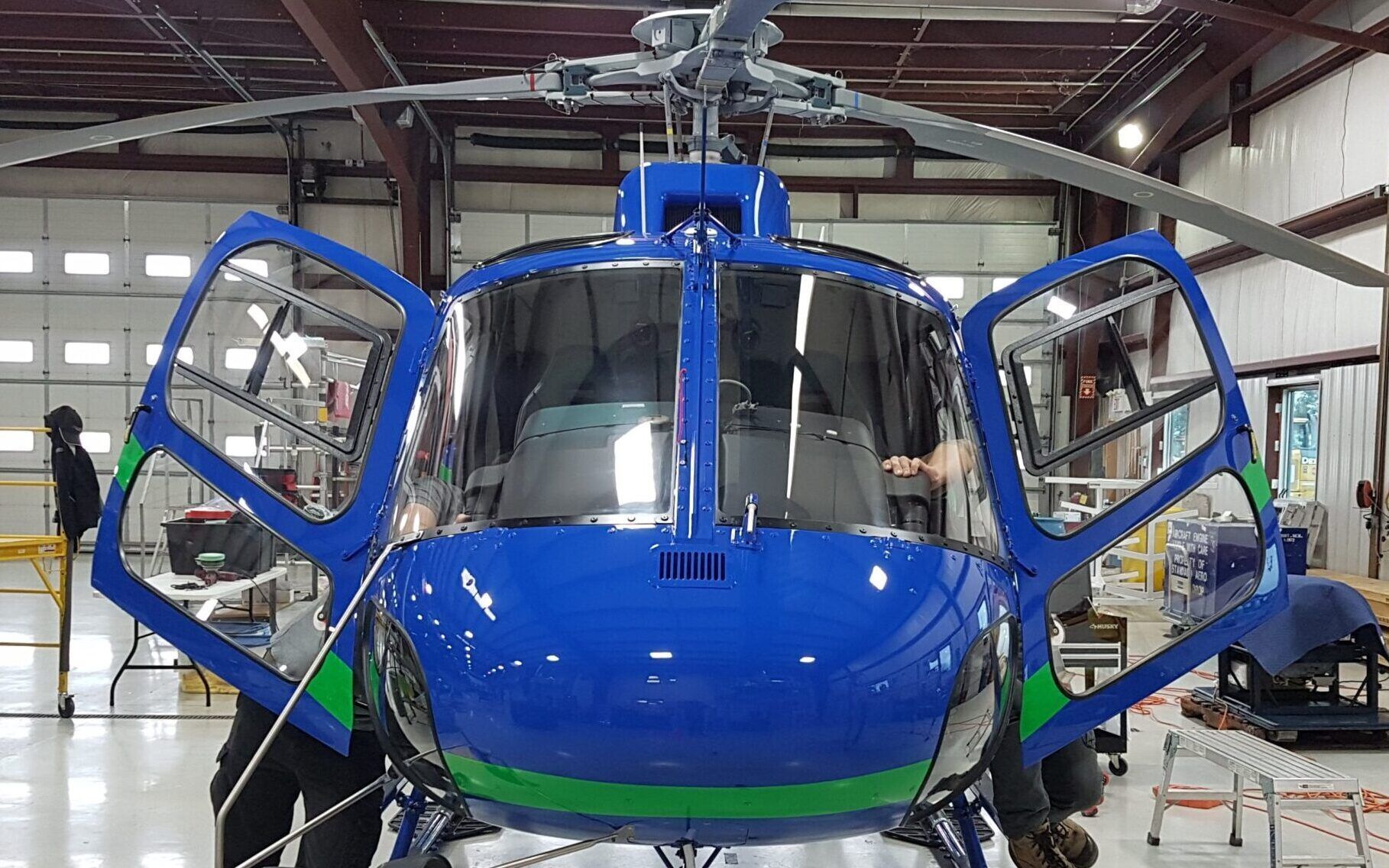 Blue helicopter with open doors in a hangar; green accents.