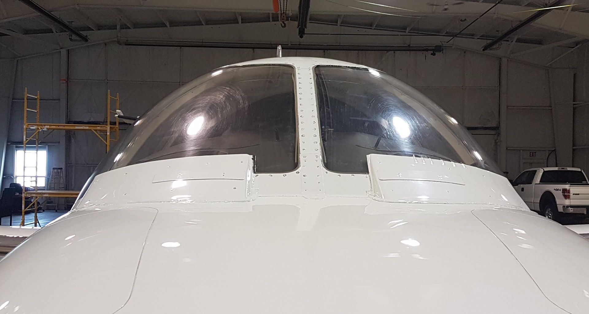 White aircraft cockpit dome. Transparent windows, white frame, hangar setting.