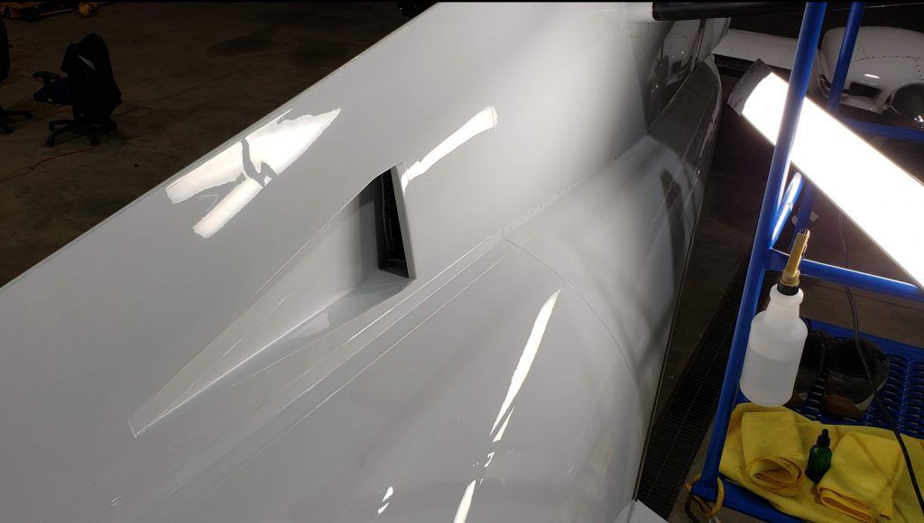 White car body being polished, with reflections and a spray bottle on a cart.