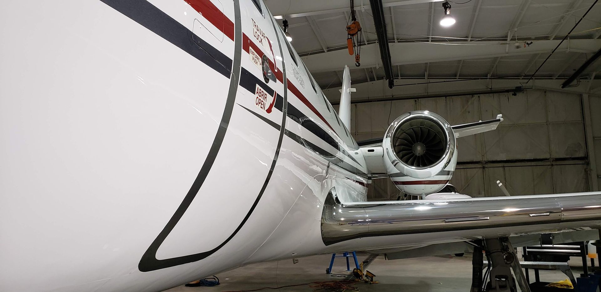 Side view of a white private jet in a hangar, featuring its engine, wing, and exterior design.