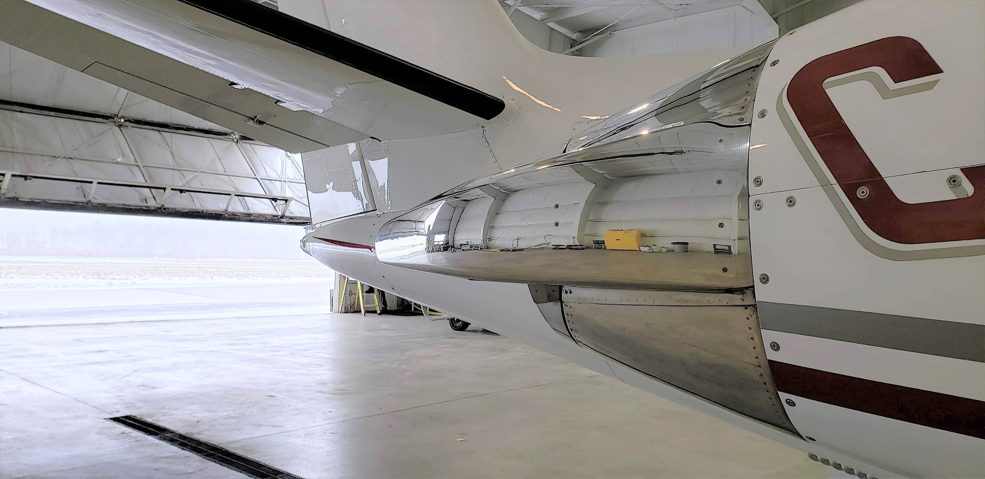 Aircraft wing with open panels, inside a hangar. Silver with maroon accents.