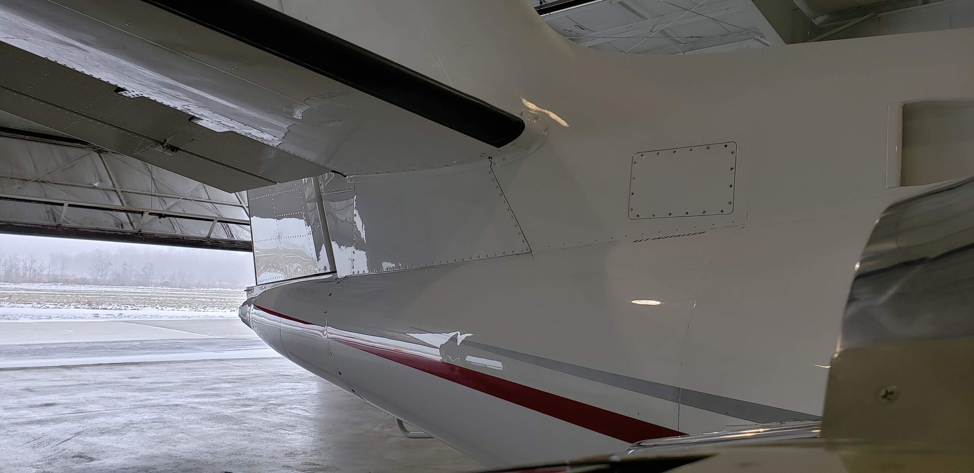 Close-up of a white aircraft fuselage with a red stripe and a partially open wing.