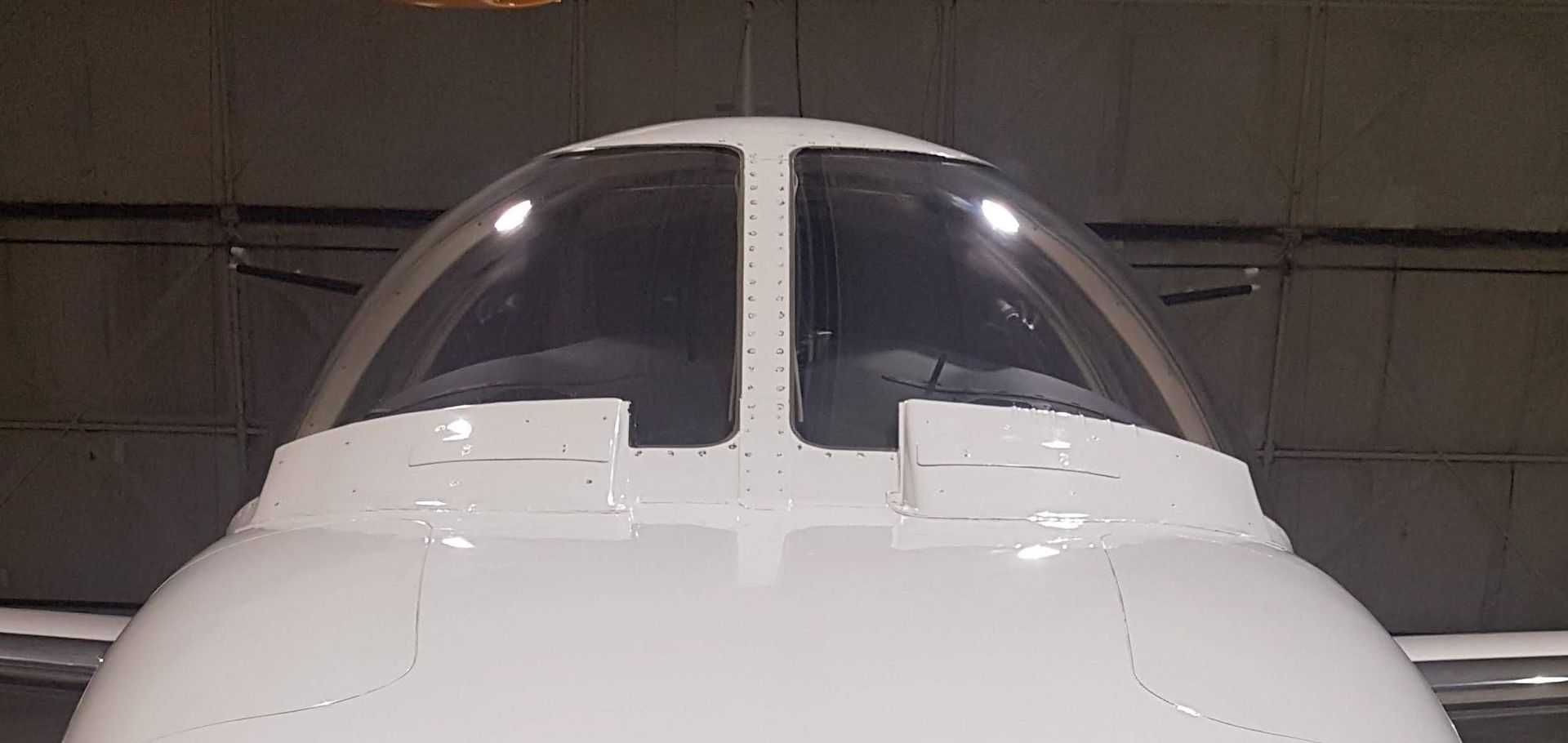 Close-up of the cockpit of a white airplane inside a hangar.