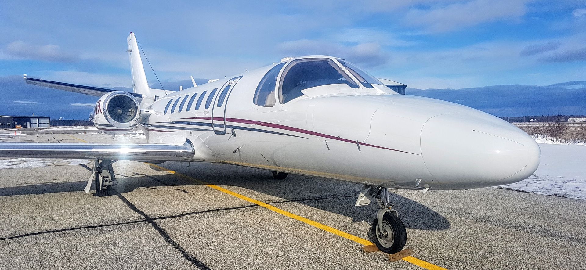 White private jet parked on a paved runway with a blue sky background.