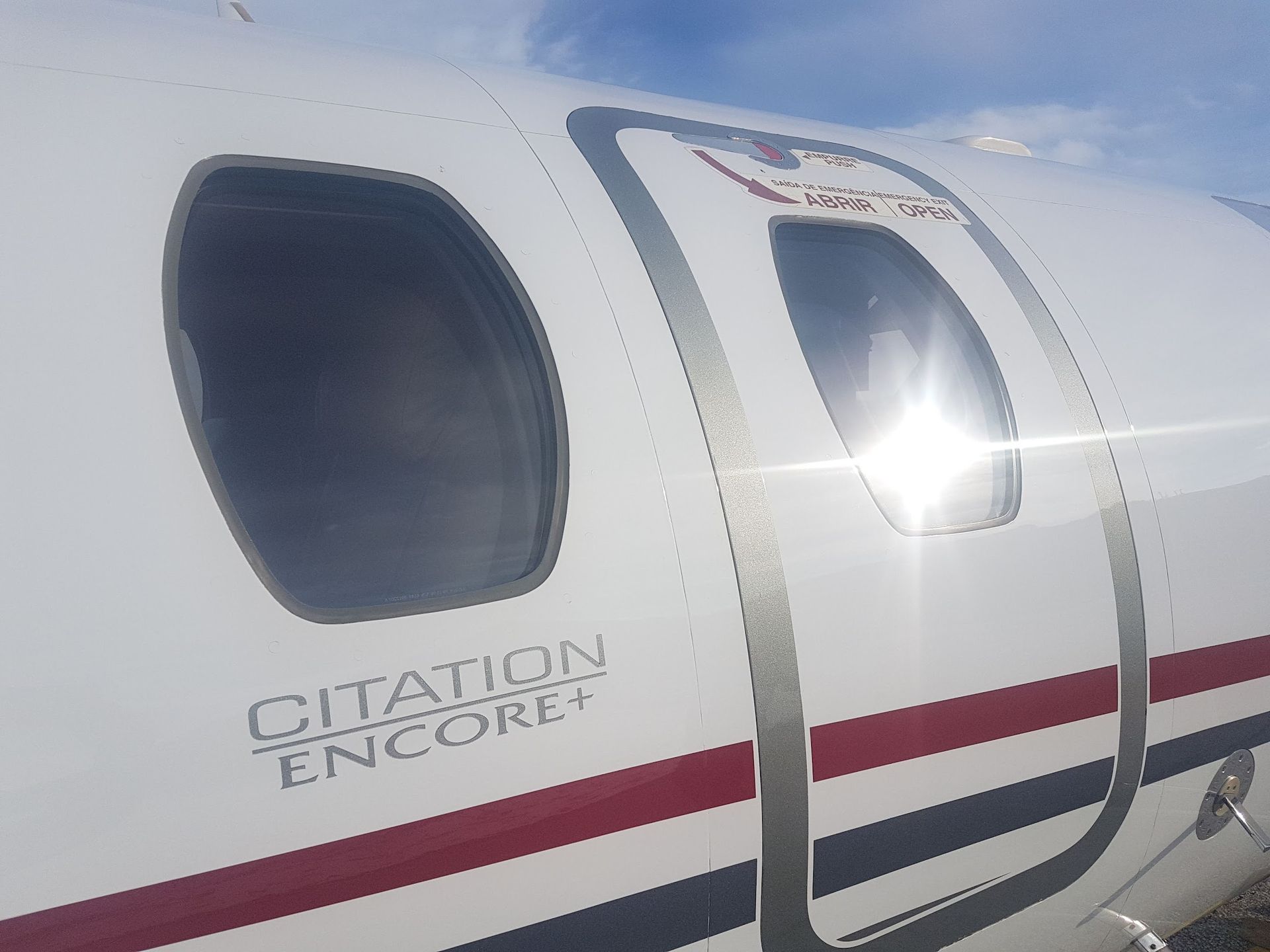 Close-up of a white Citation Encore+ airplane with two windows and sunlight reflecting off the glass.