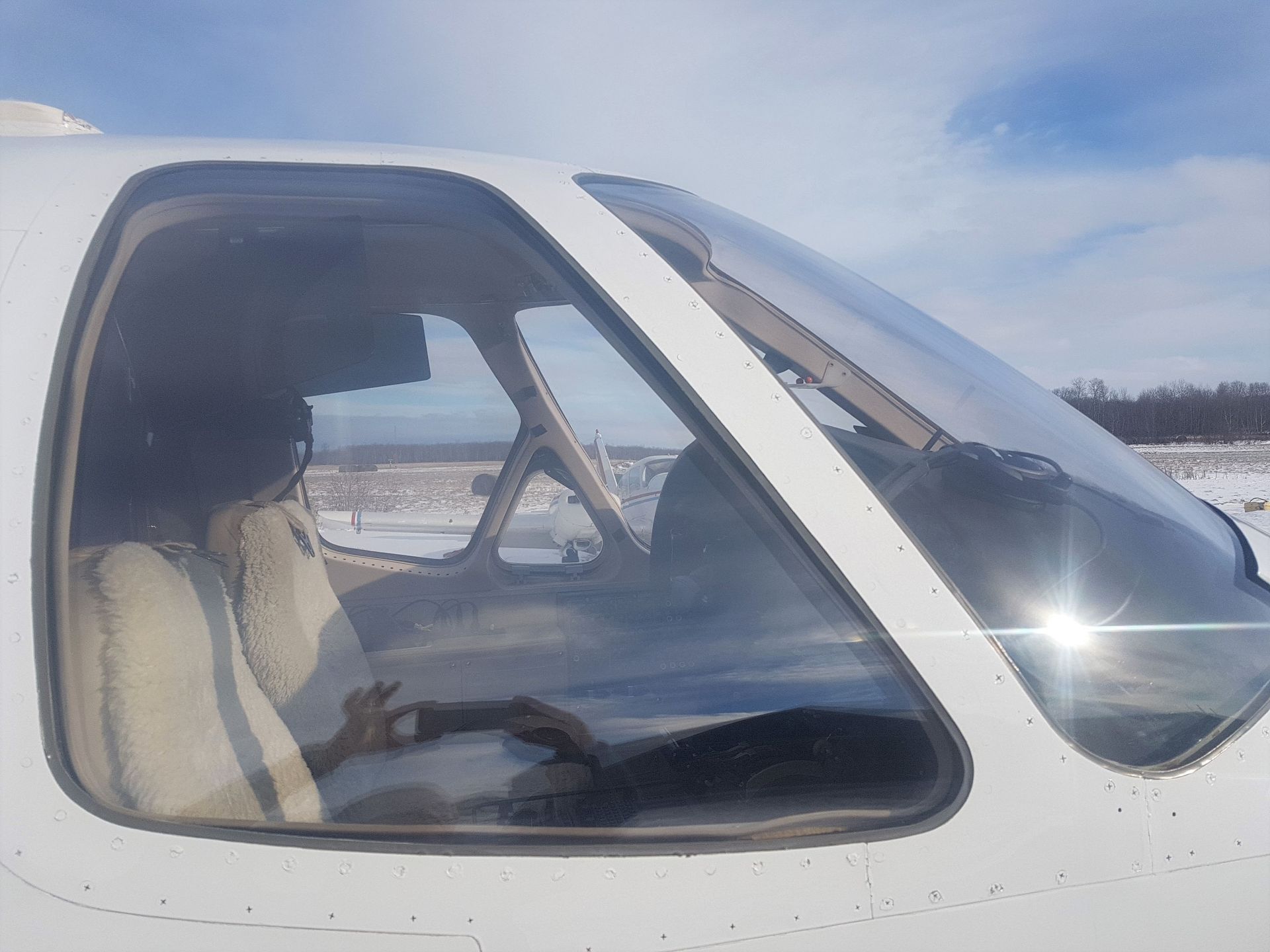 A view through the cockpit window of a small airplane, revealing the interior and winter landscape.