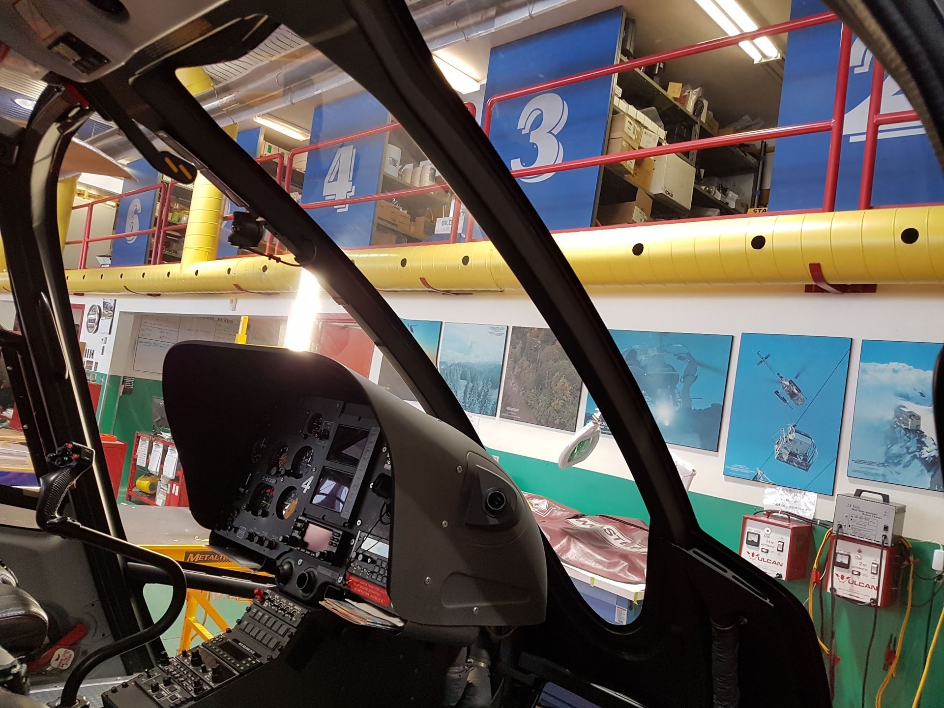Inside a helicopter cockpit, looking outward toward a workshop.