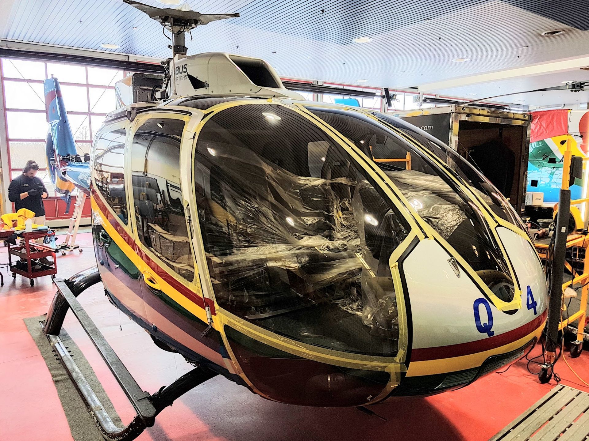 Helicopter inside a hangar with partially visible seats. White, yellow, and red stripes along the side.