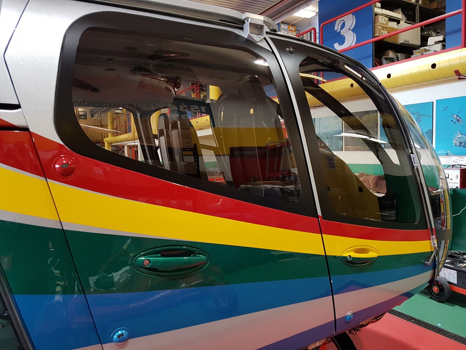 Helicopter side with rainbow stripes, parked inside a building.