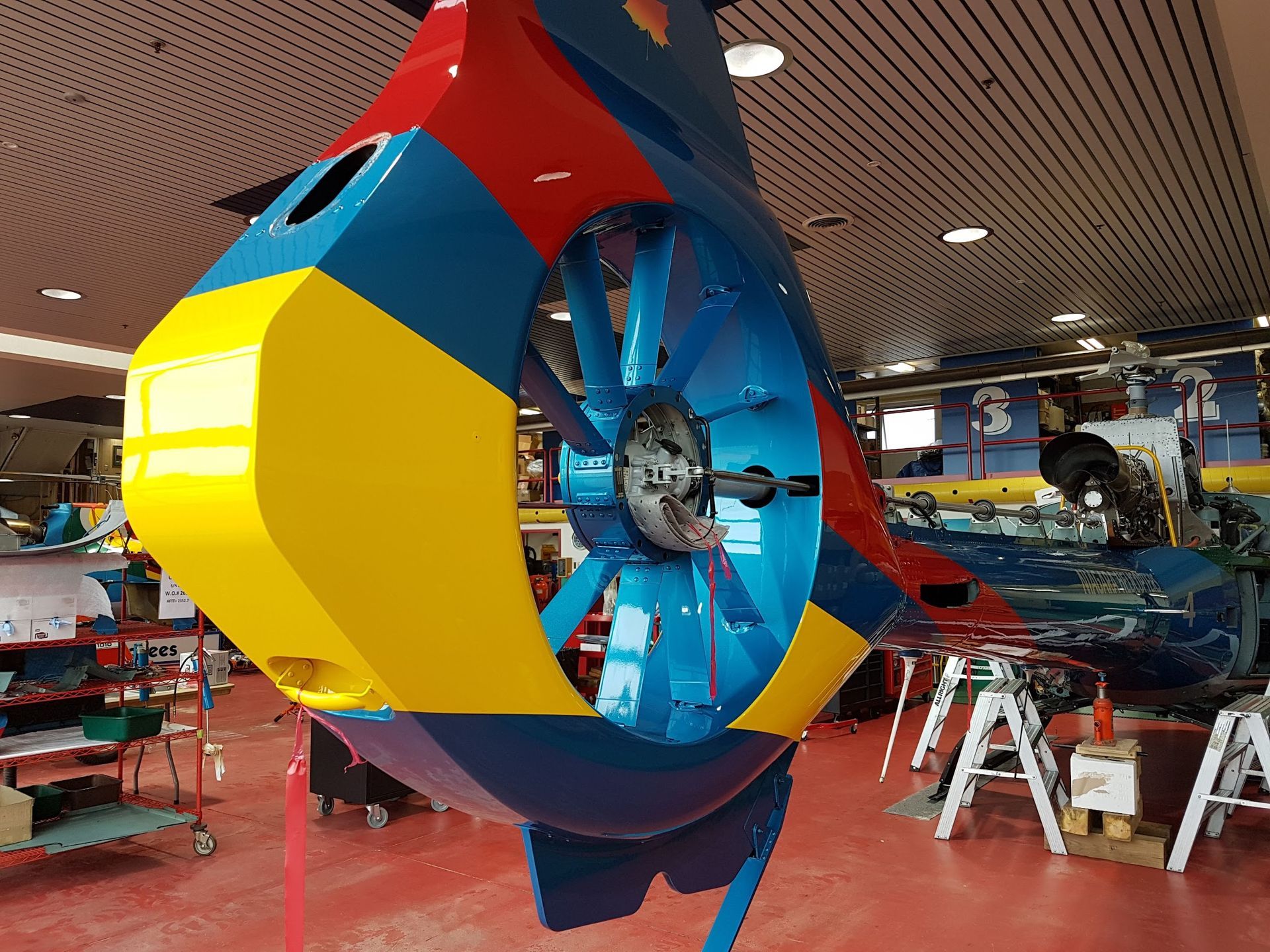 Brightly colored helicopter tail rotor in a hangar, featuring yellow, blue, and red panels.