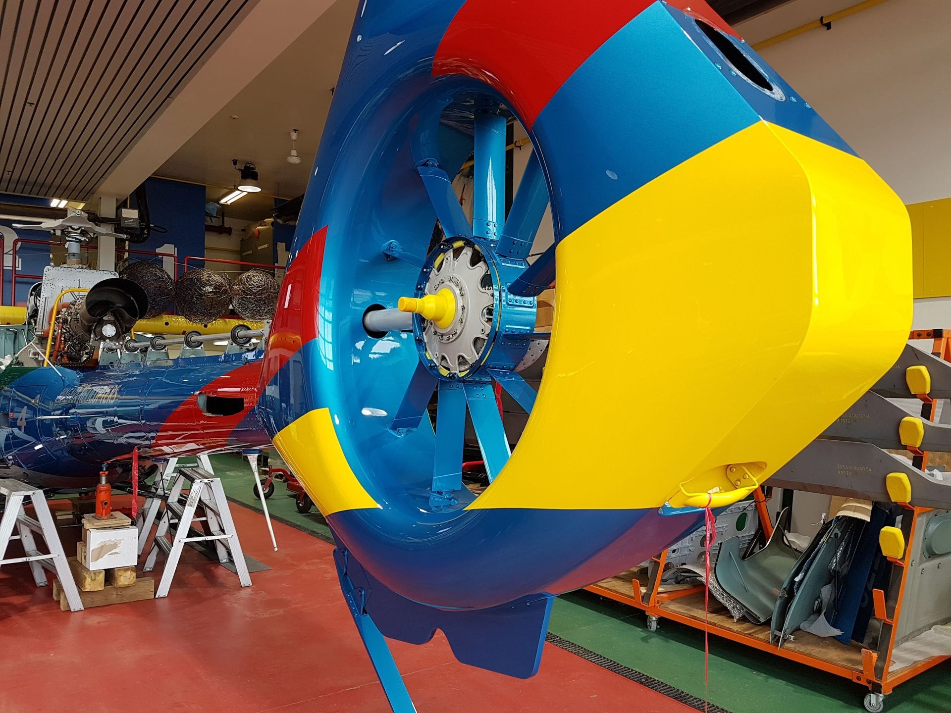 Brightly colored helicopter tail rotor in a hangar. Blue, red, and yellow paint.