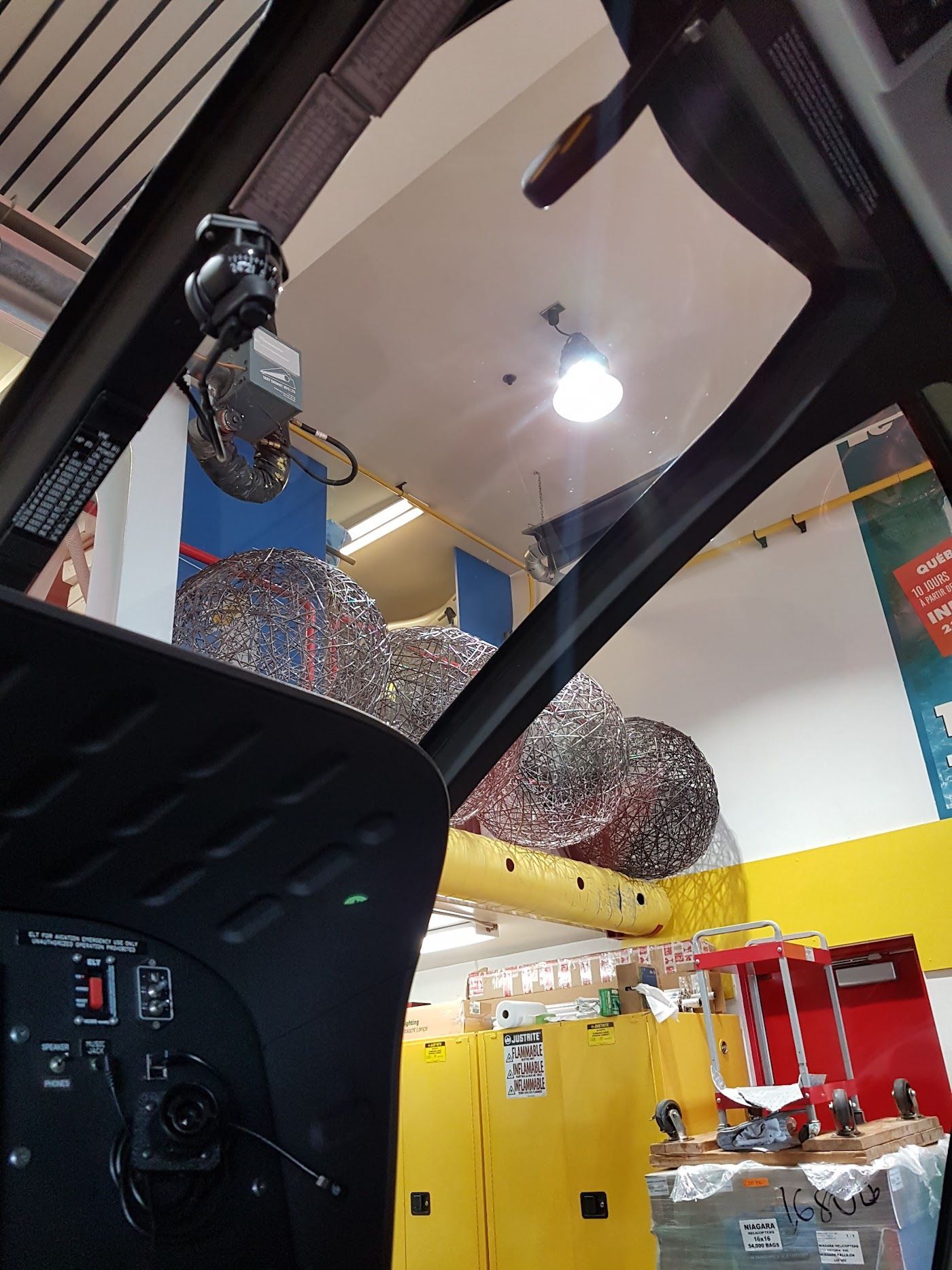 Interior of a helicopter cockpit, view past the controls and upper frame to warehouse storage.