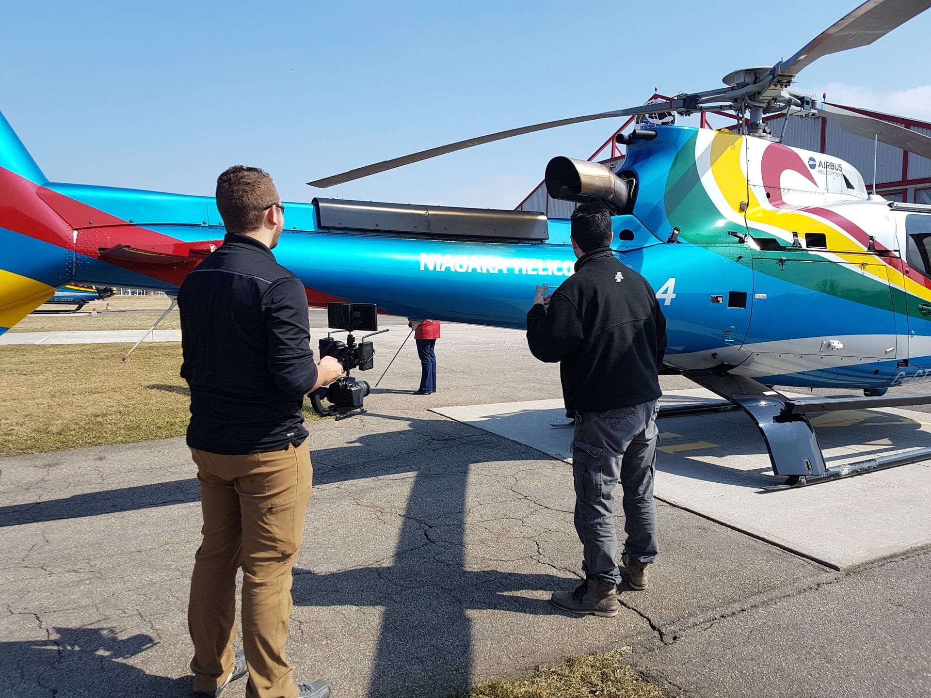Two people filming a colorful helicopter on a sunny day.