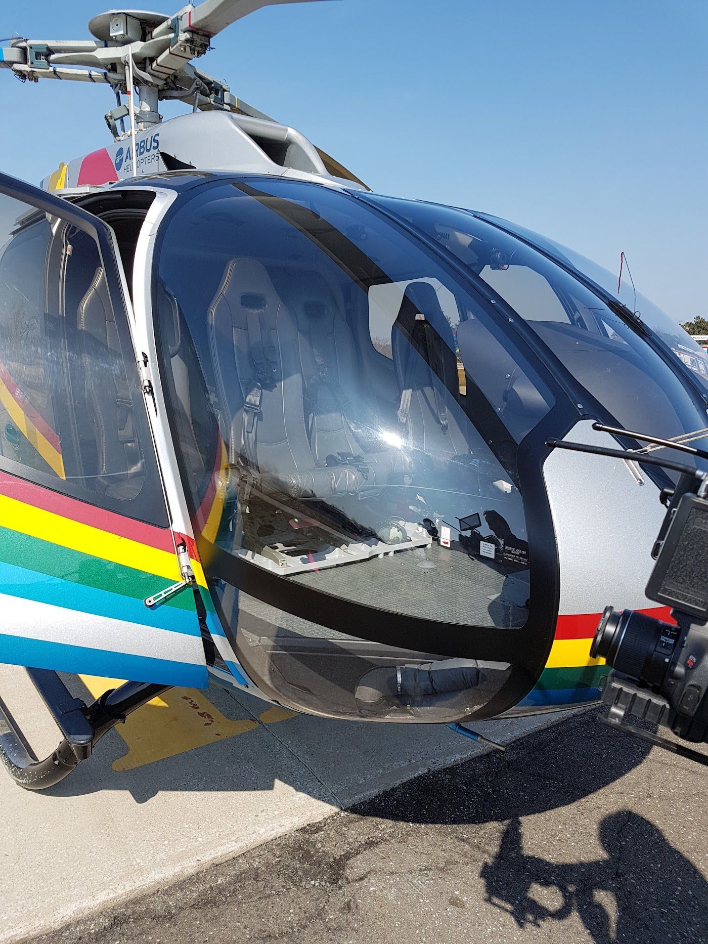 Helicopter cockpit, door open. Black, blue, yellow, and red trim. Clear window.