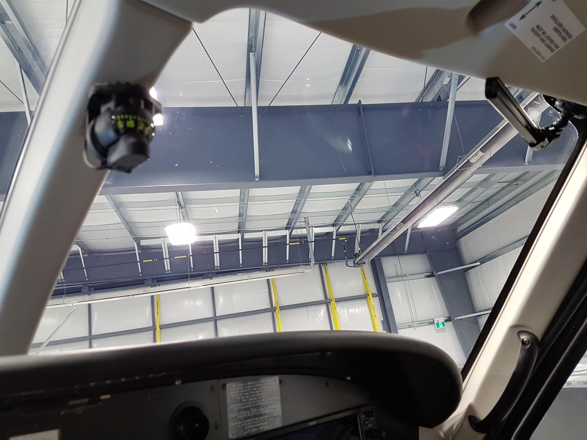 Interior view of an airplane cockpit looking out at a large hangar with blue ceiling and white walls.