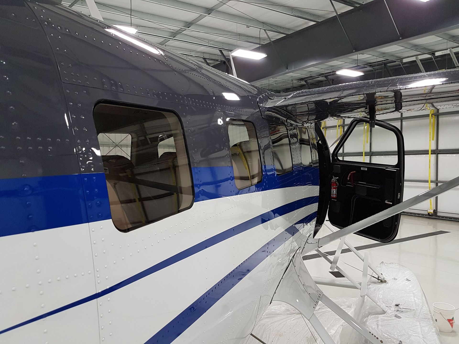 Side view of a partially assembled airplane inside a hangar. Dark blue, white, and gray body. Open door.