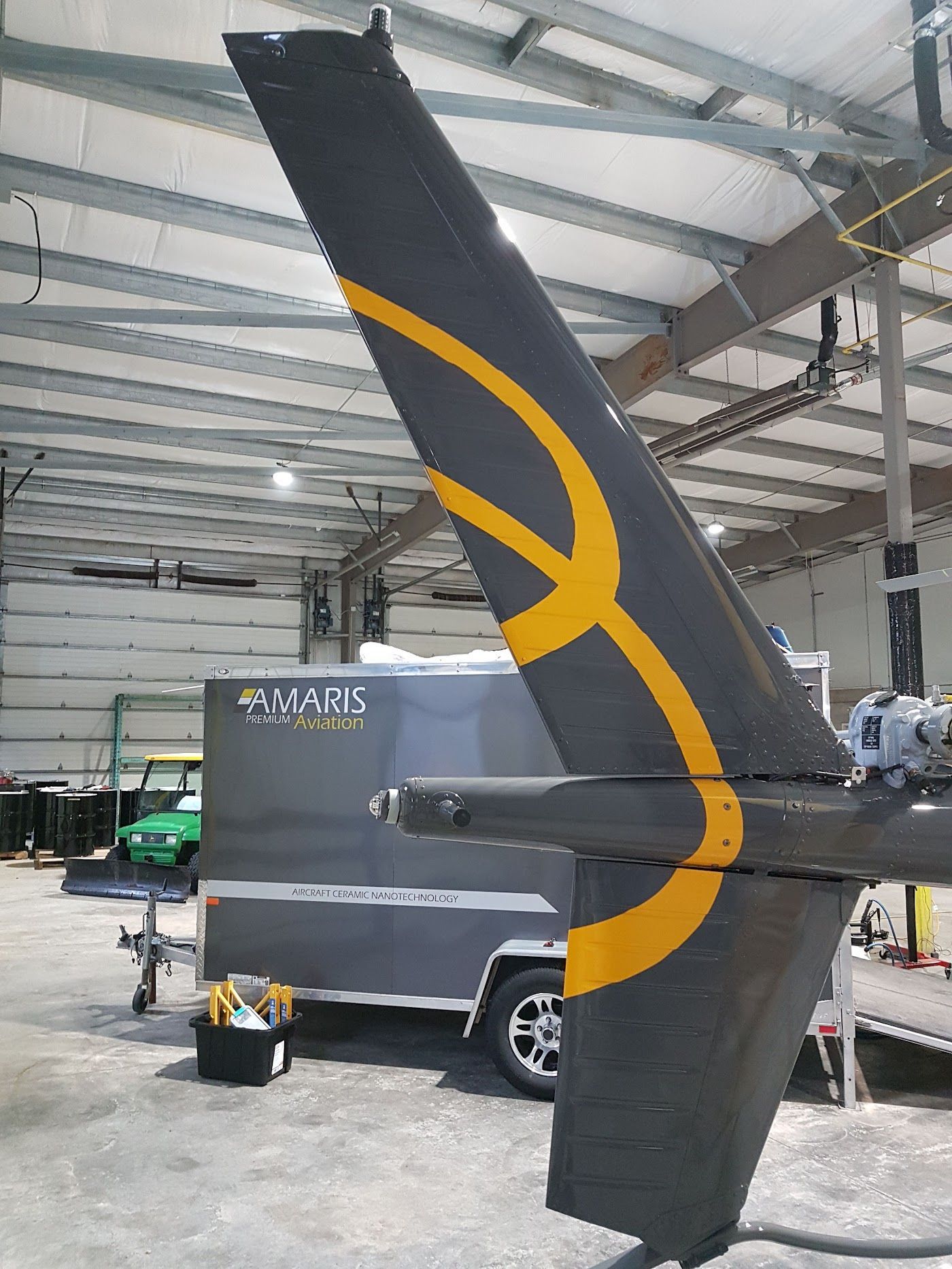 Tail fin of an aircraft with a yellow design, in a hangar with a gray trailer.