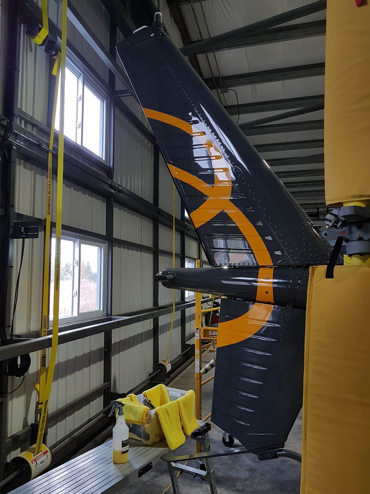 Aircraft tail, black with yellow accents, suspended in a hangar.