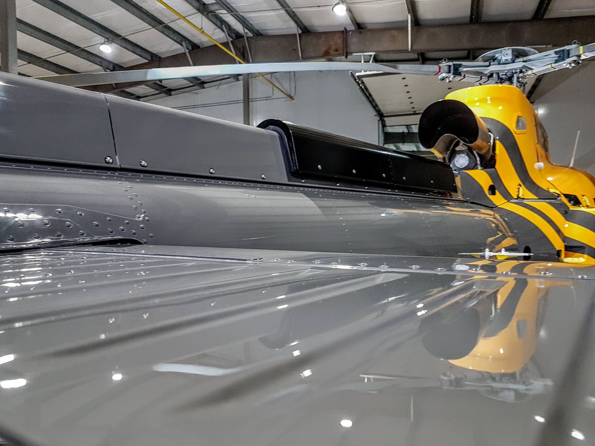 Helicopter exterior with yellow tiger-striped tail and reflective gray body in hangar.
