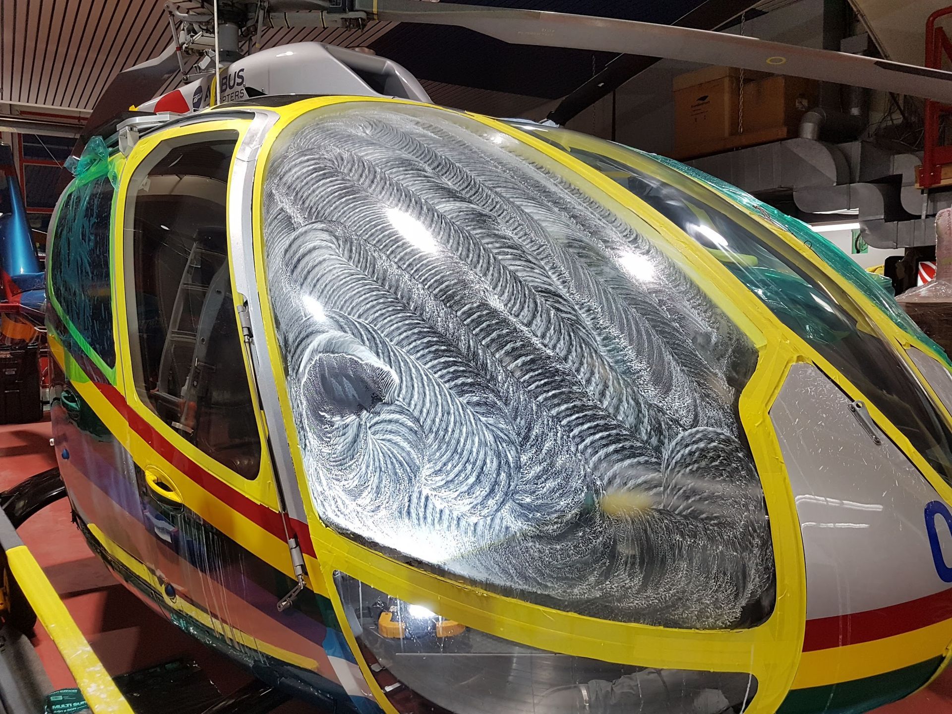 Helicopter cockpit with detailed, swirling patterns on the windshield, yellow, blue, and silver exterior.