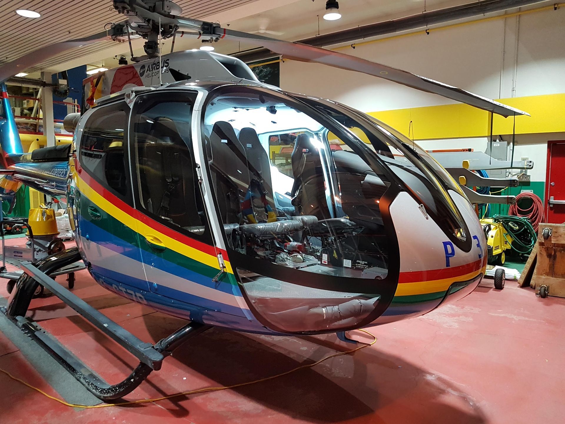 Helicopter with a rainbow stripe, parked in a hangar.