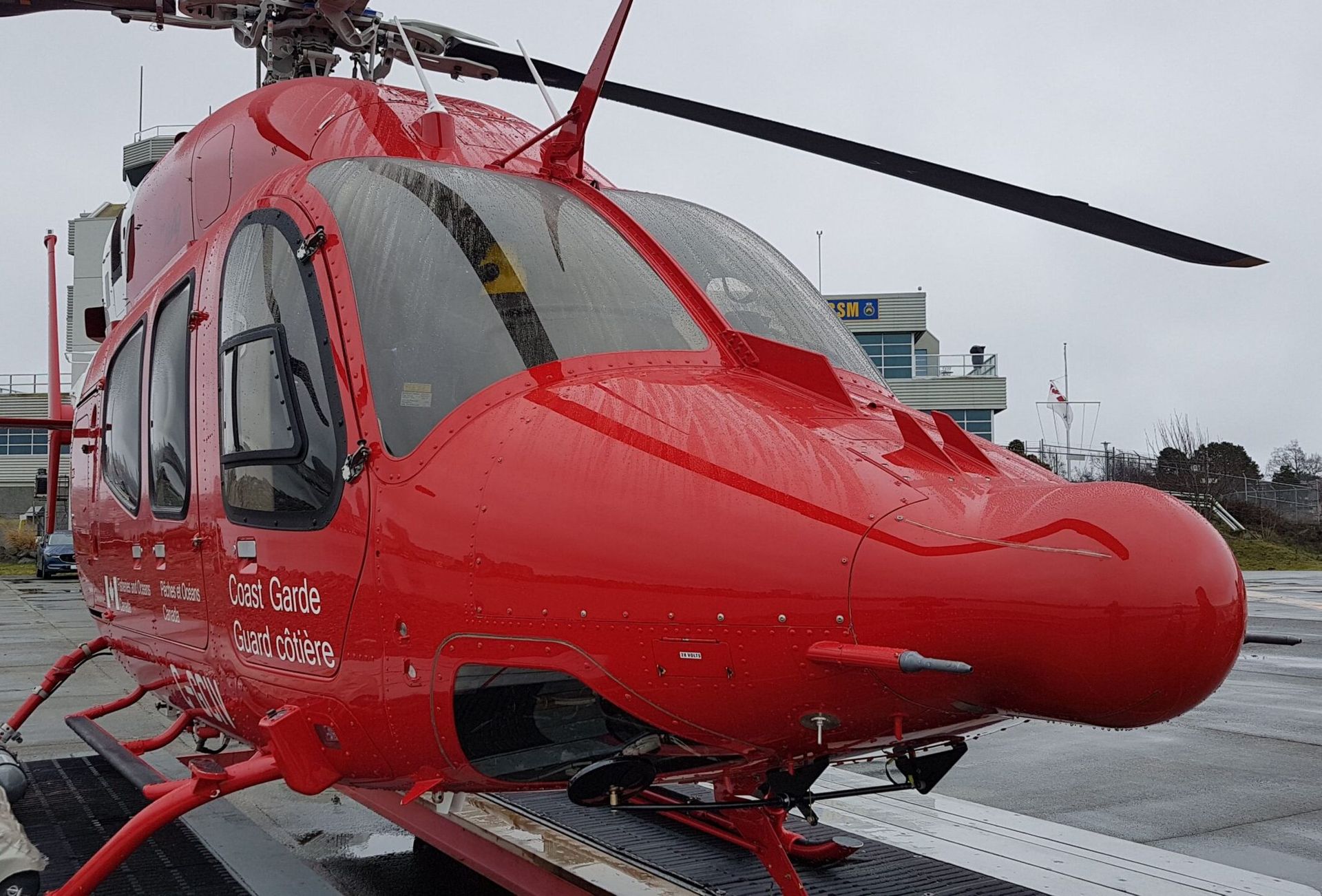 Red medical helicopter on a helipad, overcast sky.