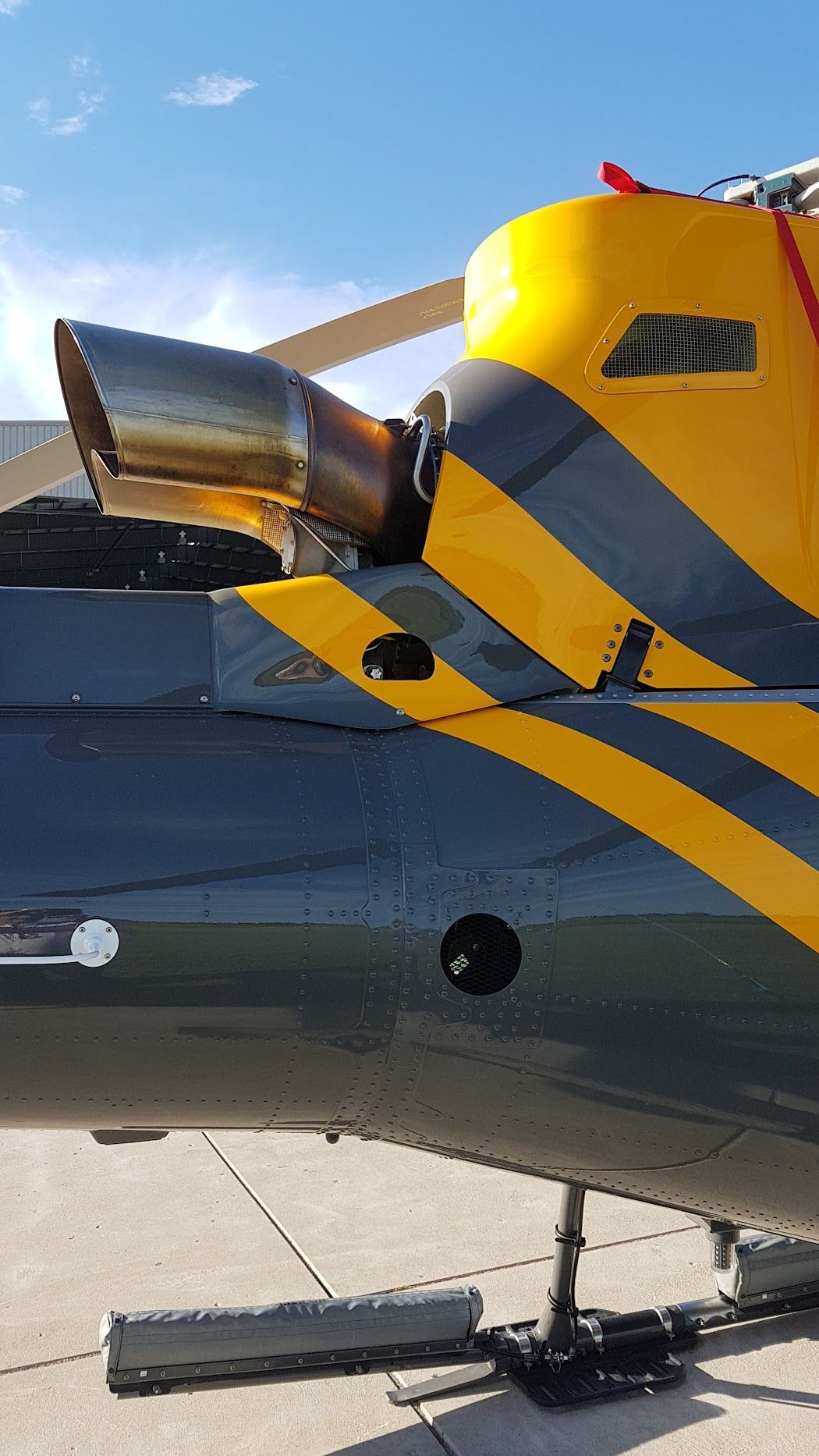 Helicopter tail detail, yellow and black stripes, exhaust visible, parked on concrete.